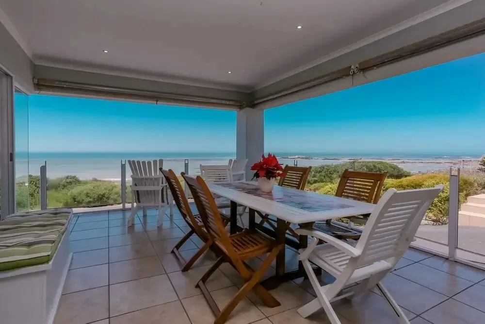 Une table à manger est placée sur une terrasse carrelée avec vue sur la mer.