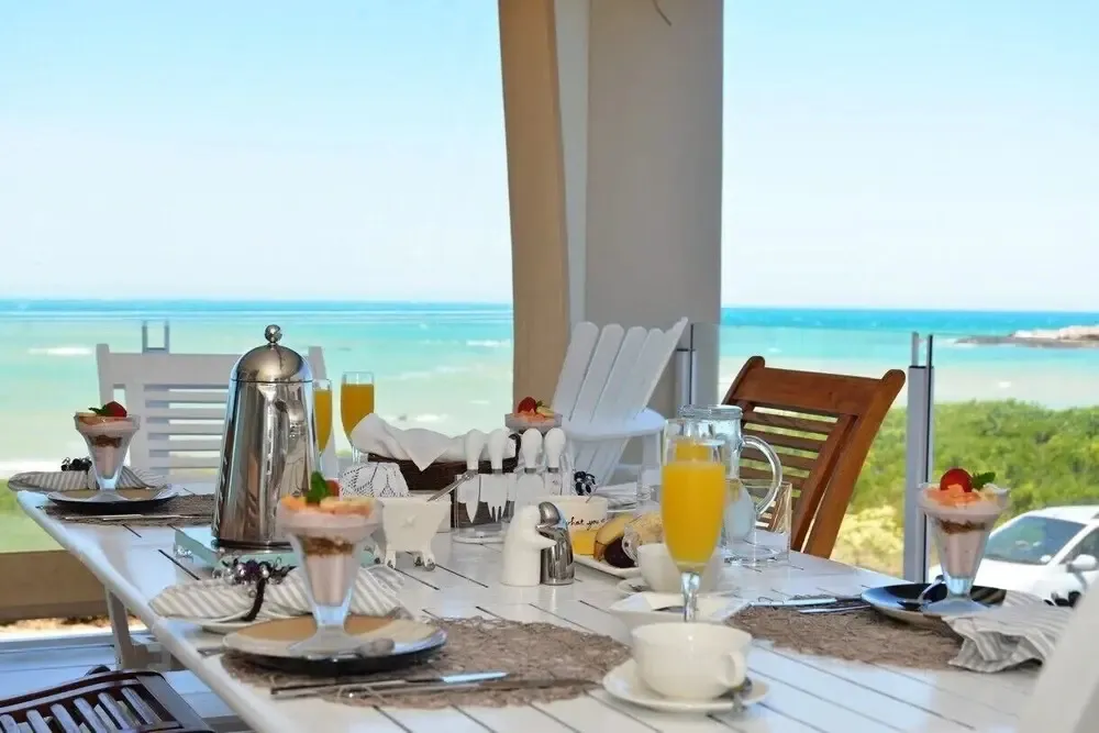 Une table est dressée avec des couverts et des plats de petit-déjeuner face à la mer.