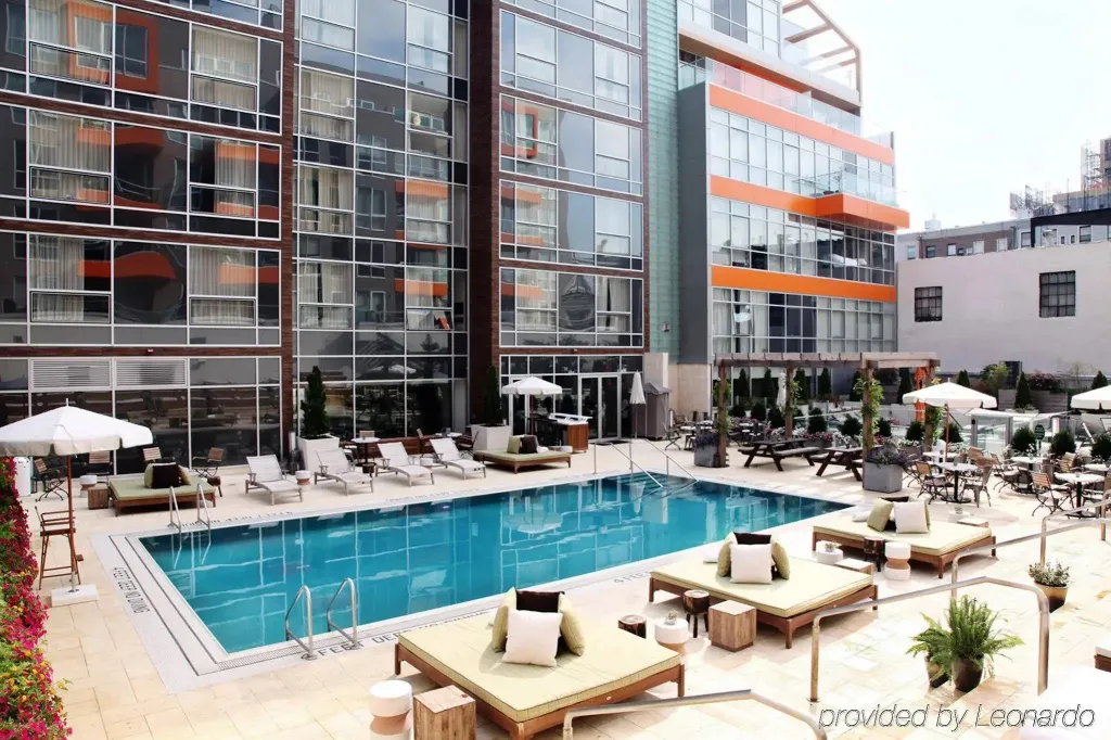 Une piscine rectangulaire bordée de transats et de parasols, devant un bâtiment moderne.