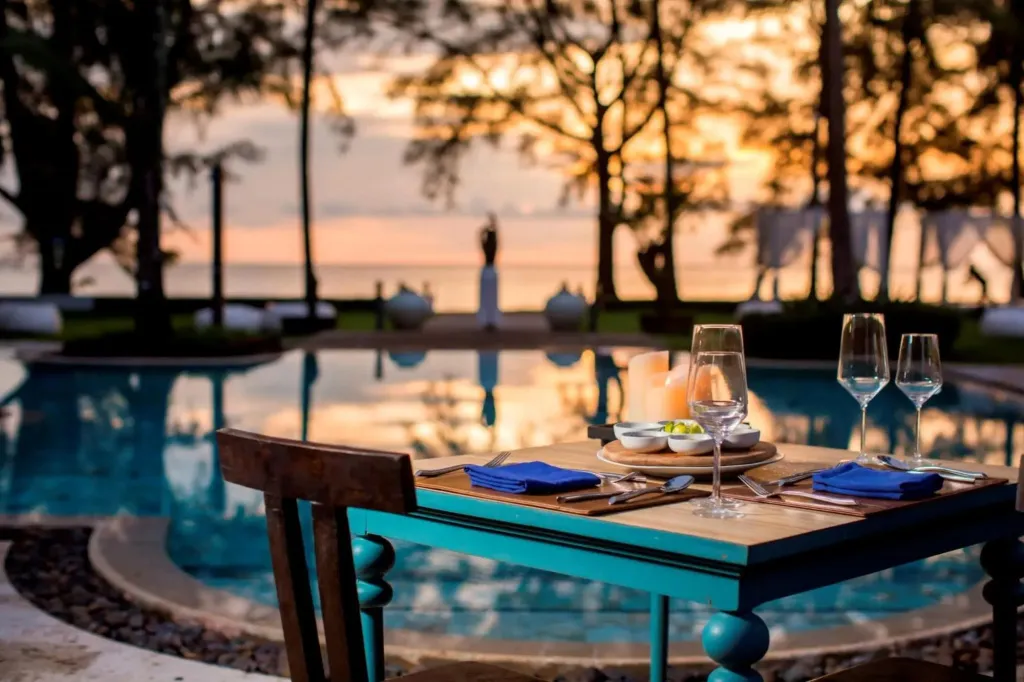 Table dressée au bord d'une piscine au coucher du soleil.