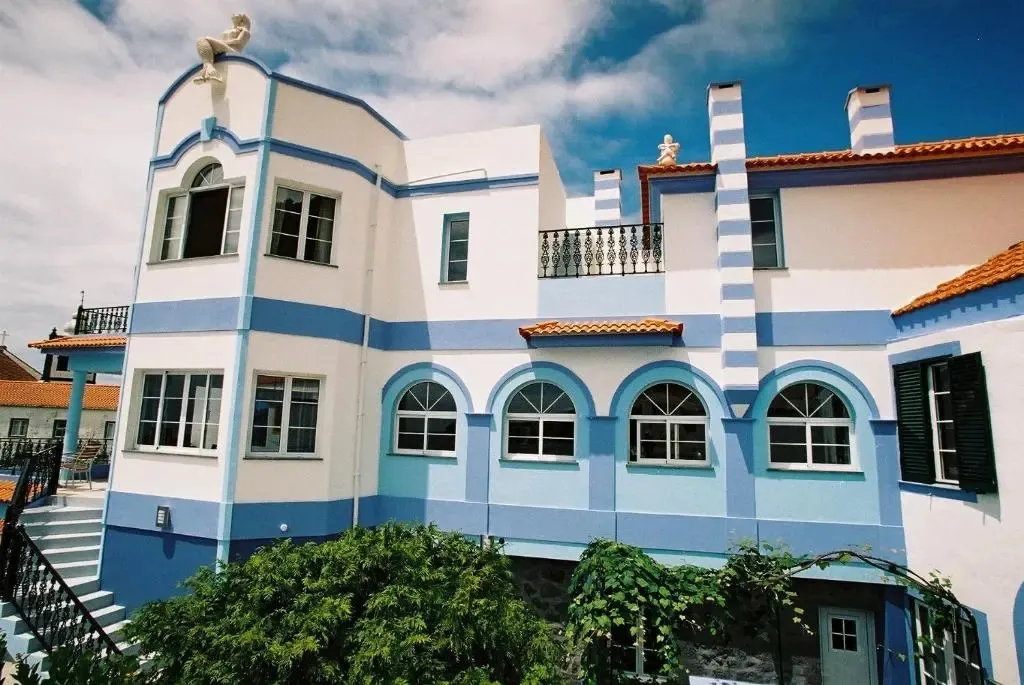 Facade d'un bâtiment aux couleurs vives avec des fenêtres en arc et un toit en tuiles.