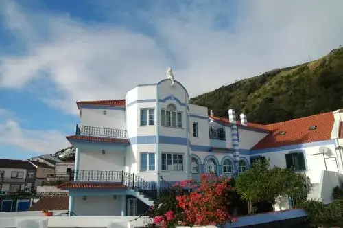 Bâtiment blanc et bleu avec des balcons fleuris, situé sur une colline verdoyante.