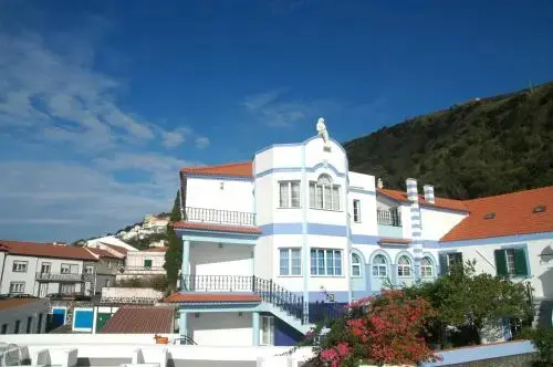 Bâtiment blanc et bleu avec des balcons et des toits rouges, surplombant un paysage urbain.