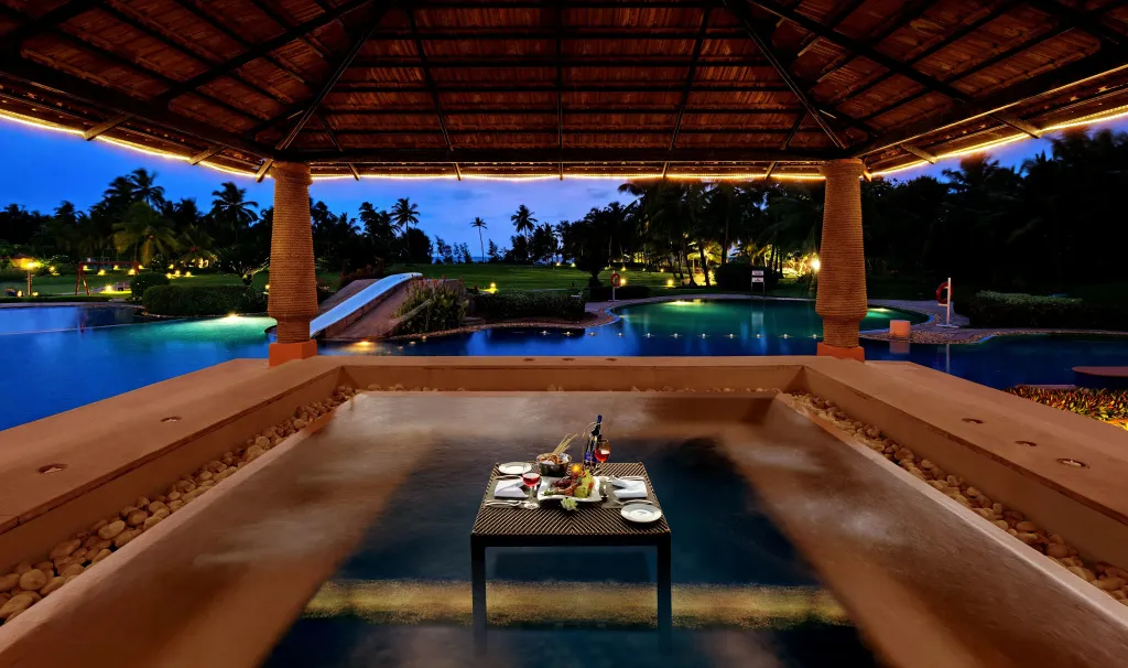 Table dressée pour un repas en extérieur avec vue sur une piscine illuminée au crépuscule.