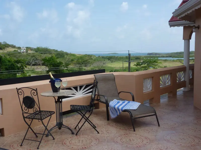 Une terrasse ensoleillée offre une vue sur un paysage verdoyant et la mer.