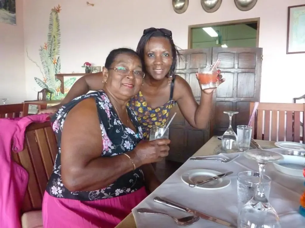 Deux femmes sourient en tenant des verres sur une table dressée dans une salle à manger.