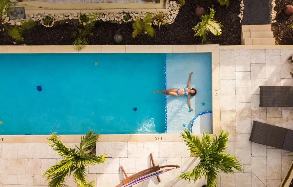 Une personne flotte sur le dos dans une piscine rectangulaire entourée d'une terrasse.
