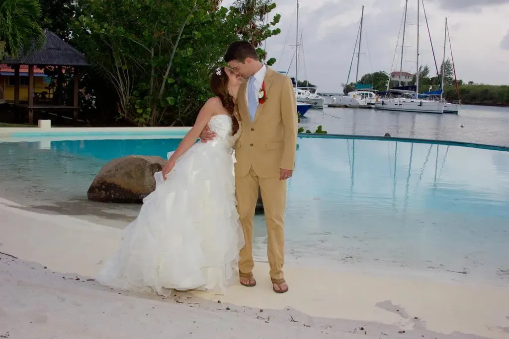 Un couple s'embrasse près d'une piscine turquoise bordée de sable blanc.