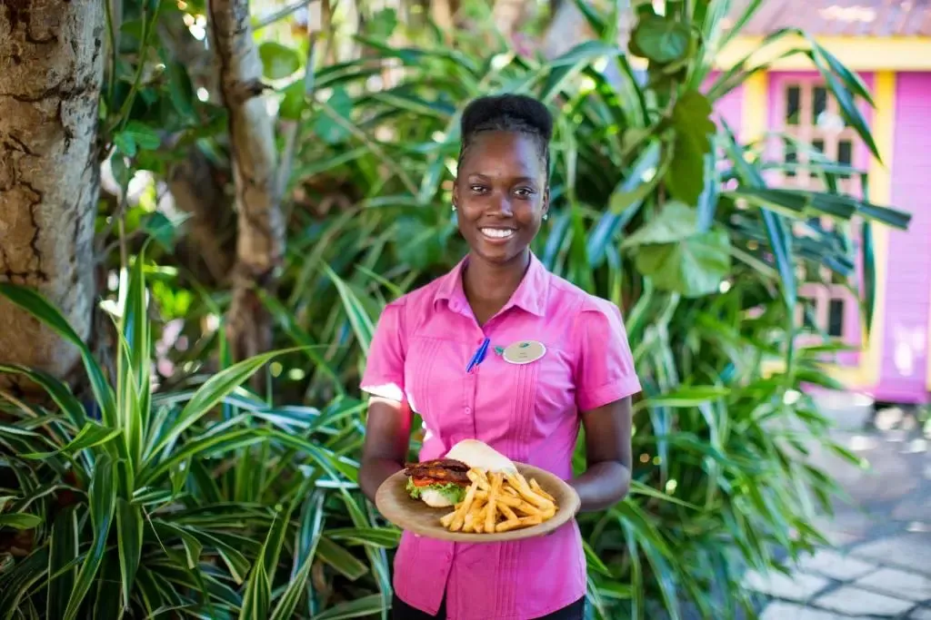 Une personne souriante présente un plat de frites et un sandwich.