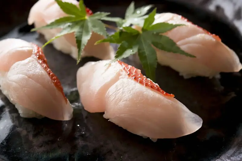 Plusieurs sushis au poisson cru sont présentés sur une assiette noire.