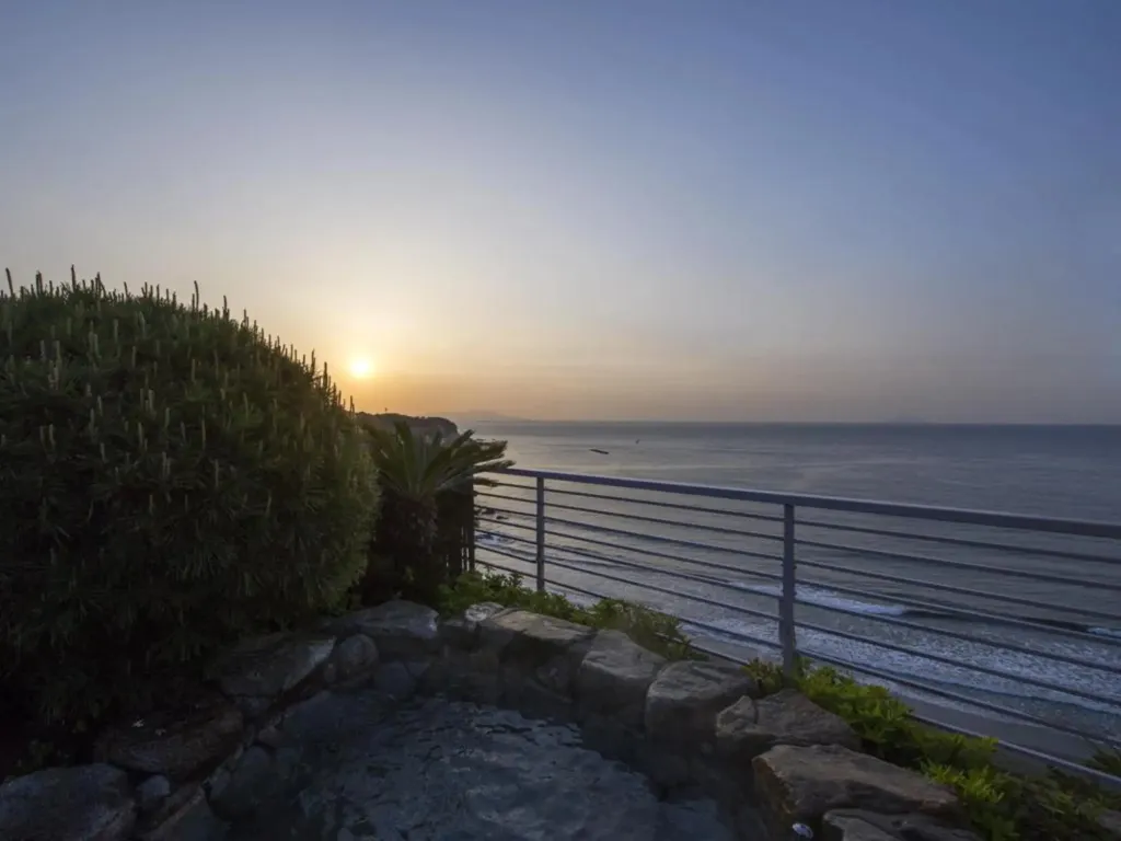 Vue sur la mer au coucher du soleil depuis une terrasse rocheuse.