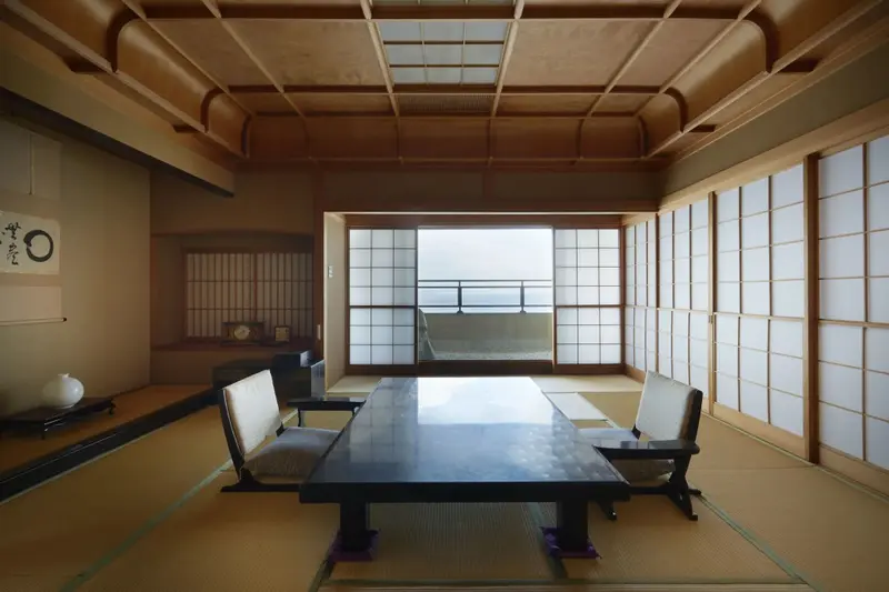 Une pièce lumineuse avec une table basse et des coussins de sol, donnant sur un paysage brumeux.