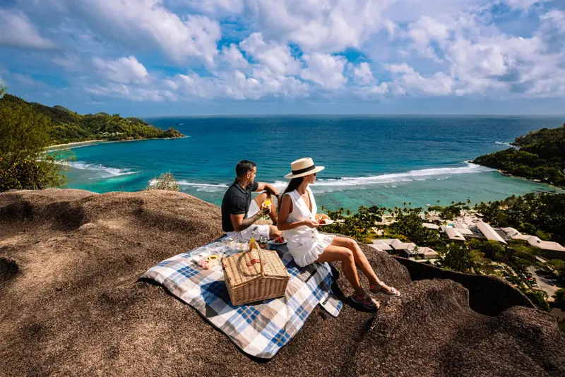 Un couple déguste un repas sur un rocher surplombant une plage.