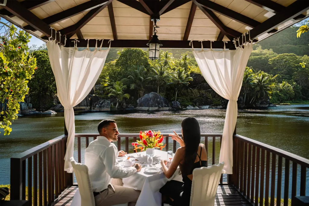 Un couple déjeune sur une terrasse ombragée avec vue sur une baie.