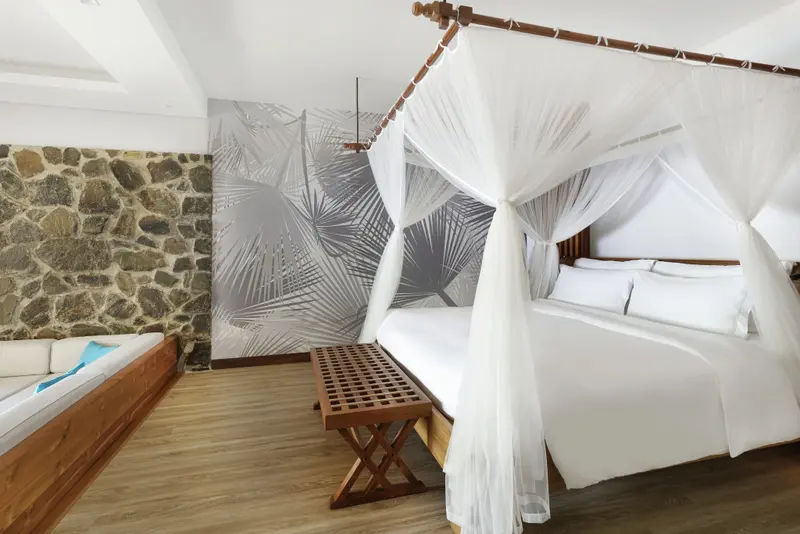 Une chambre lumineuse avec un lit à baldaquin et un mur décoré de motifs végétaux.