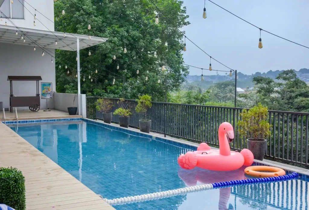 Une piscine rectangulaire avec un flamant rose gonflable flotte à côté d'une terrasse ombragée.