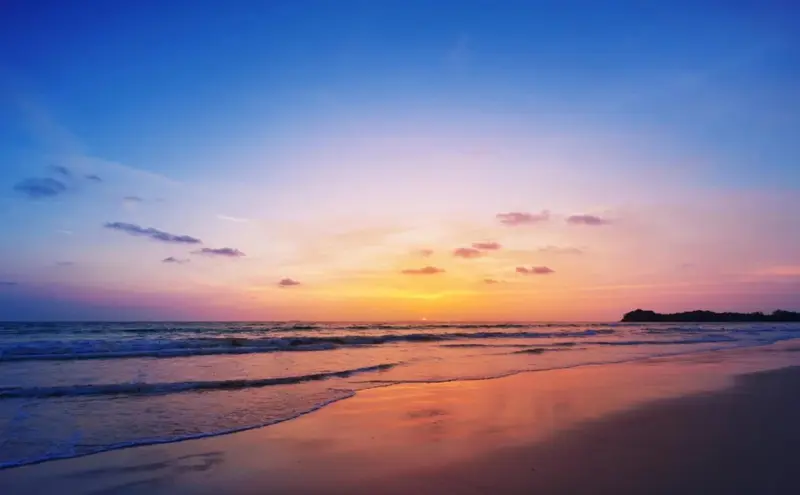 Le soleil se couche sur une plage de sable fin, illuminant la mer d'une lumière orangée.