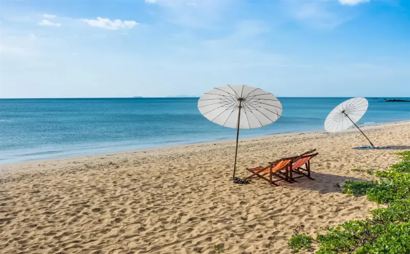 Deux transats et parasols sur une plage de sable fin bordée par une mer turquoise.