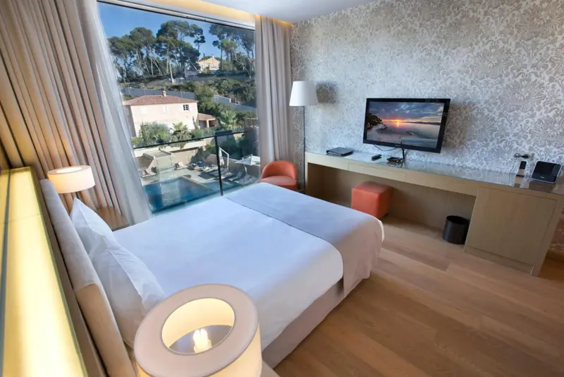 Une chambre lumineuse avec un grand lit et une vue sur une piscine et la végétation.