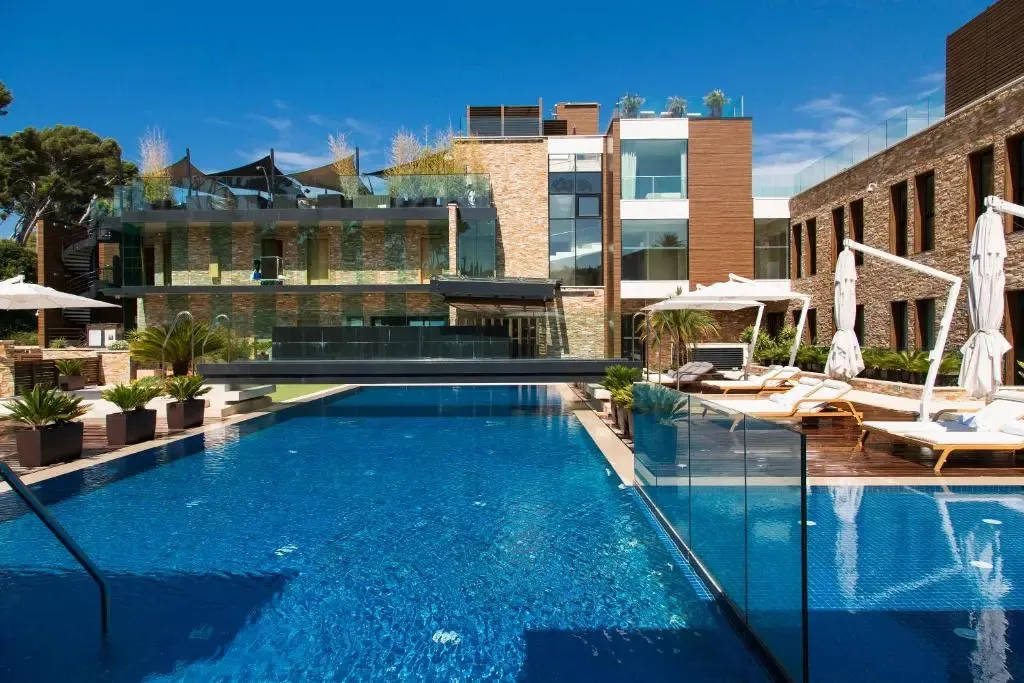 Une piscine bleue bordée de transats blancs invite à la détente devant un bâtiment moderne.