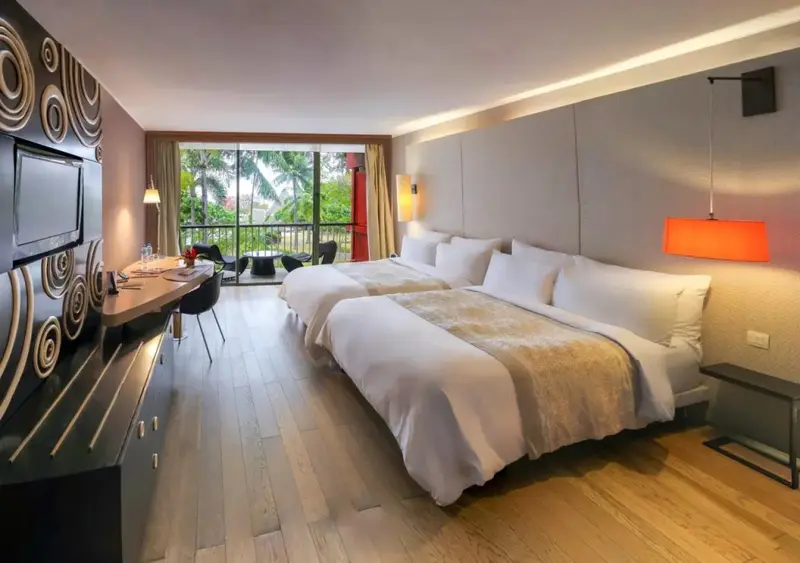 Une chambre lumineuse avec deux lits et un coin repas près d'une baie vitrée.