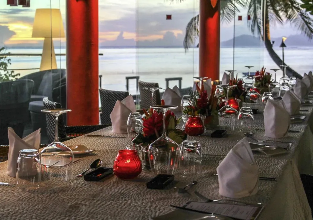 Une table dressée avec des couverts et des verres, devant une vue sur la mer au coucher du soleil.
