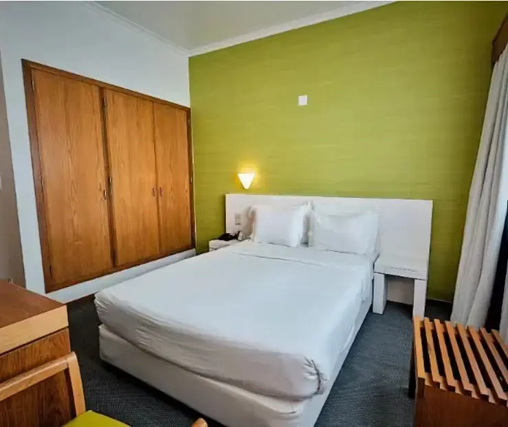 Une chambre lumineuse avec un grand lit blanc et un mur vert.