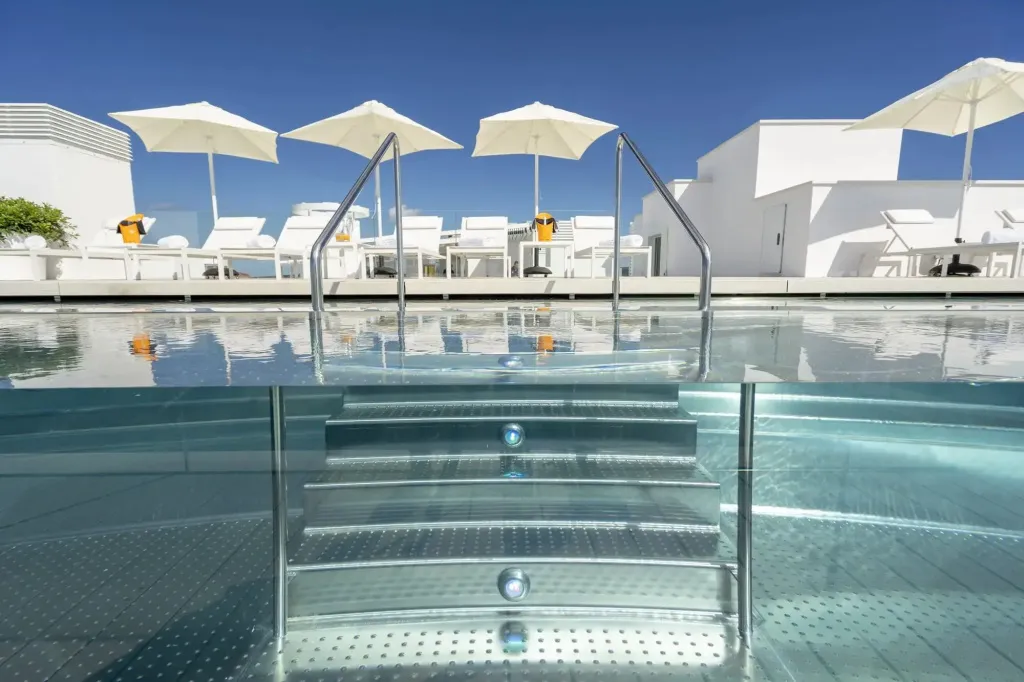 Une piscine à débordement avec des transats blancs et des parasols.