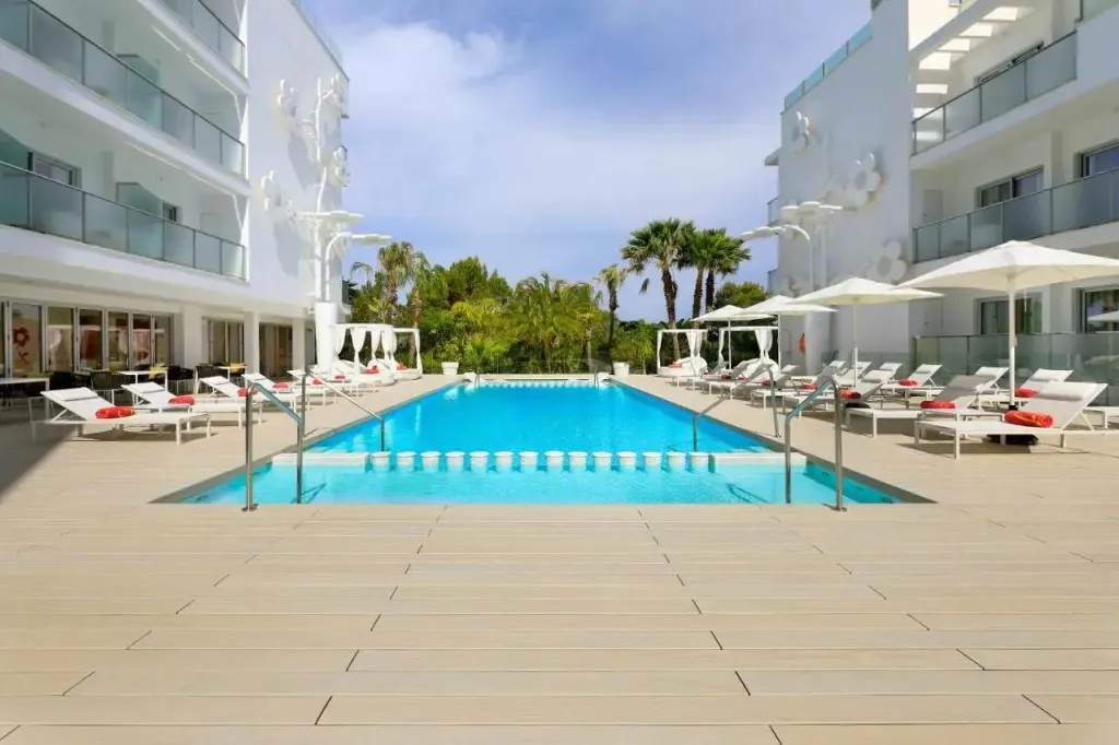 Une piscine rectangulaire bordée de transats blancs sous des parasols.