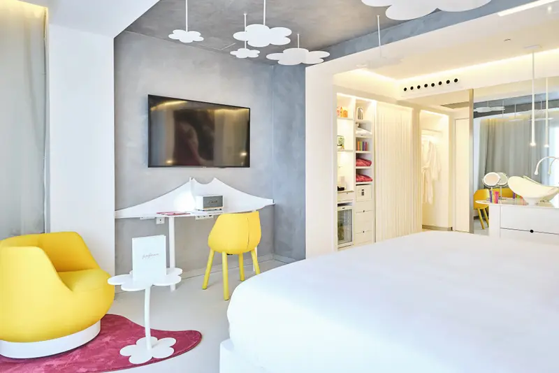Une chambre lumineuse avec un lit blanc et des meubles jaunes.