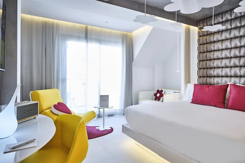 Une chambre lumineuse avec un lit blanc et un fauteuil jaune.