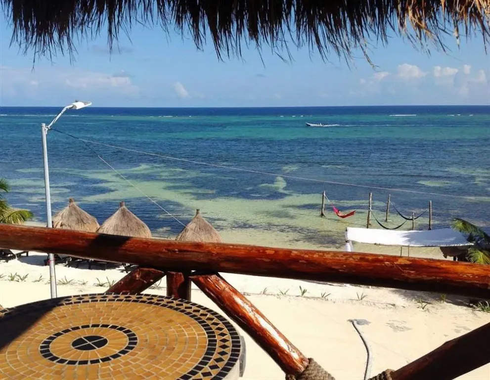 Vue sur une plage de sable blanc et une mer turquoise depuis une terrasse ombragée.
