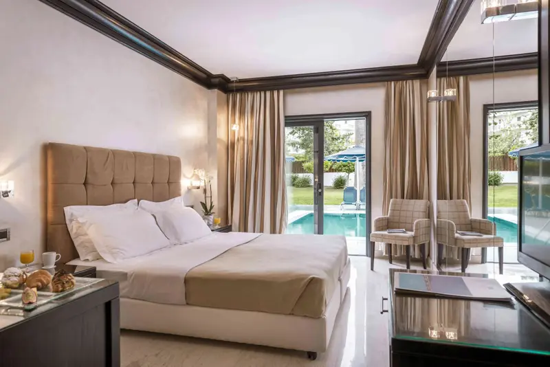 Une chambre lumineuse avec un grand lit et un coin salon donnant sur une piscine.