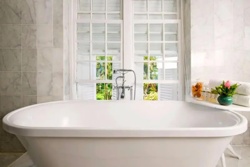 Une baignoire sur pieds se trouve devant une fenêtre à volets blancs.