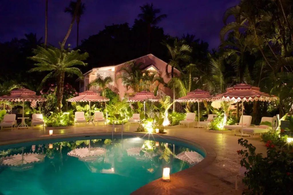 Piscine illuminée au crépuscule avec des parasols rayés et une végétation luxuriante.