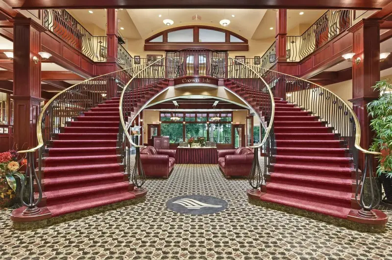 Un grand escalier en bois rouge mène à un hall d'entrée lumineux et décoré.