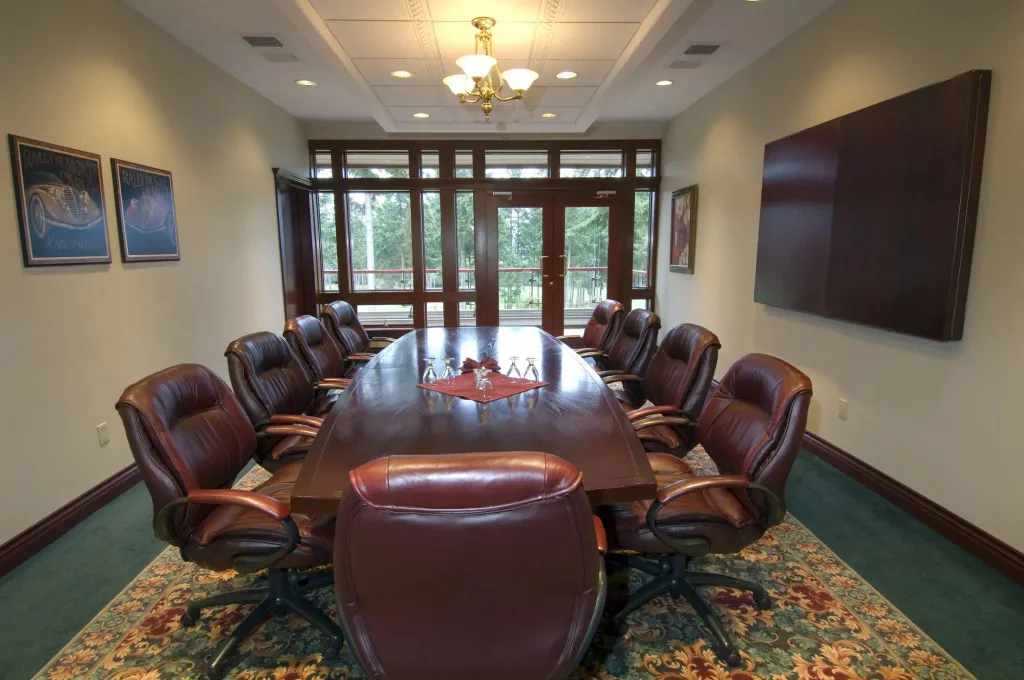 Une longue table de réunion est entourée de fauteuils en cuir dans une salle lumineuse.