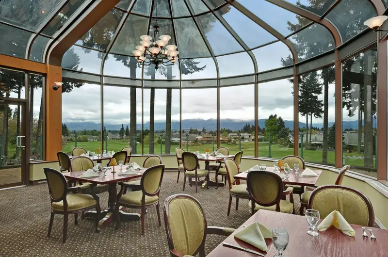 Une salle lumineuse avec des tables dressées face à un paysage verdoyant.