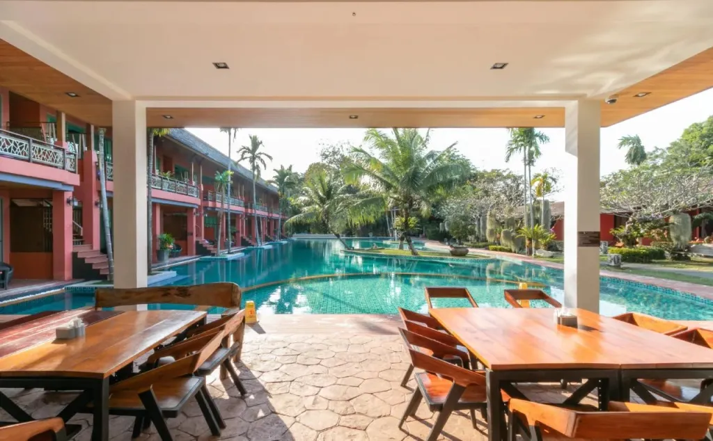 Une salle à manger extérieure surplombe une grande piscine turquoise.
