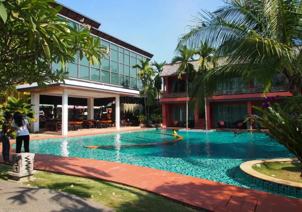 Une piscine turquoise bordée d'une terrasse et de bâtiments modernes.