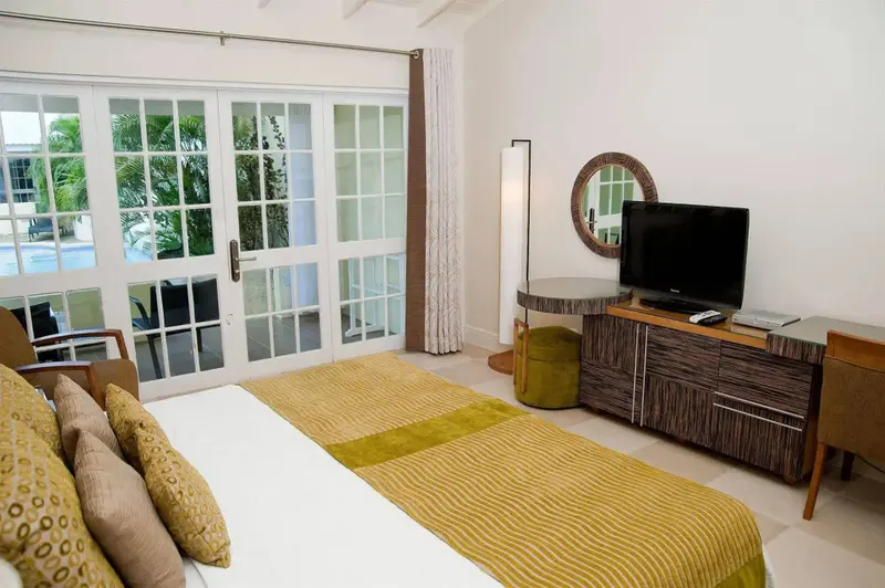 Une chambre lumineuse avec un lit recouvert d'une courtepointe jaune et verte, donnant sur une terrasse et une piscine.