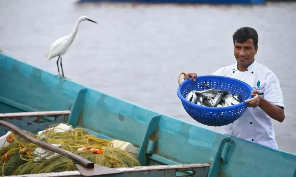 Un homme souriant présente un panier de poissons frais à bord d'un bateau bleu.