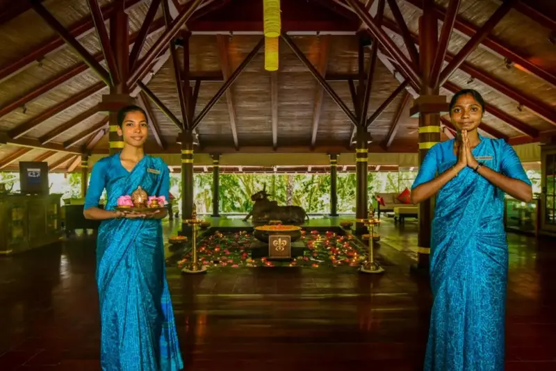 Deux femmes en tenue traditionnelle accueillent avec un plateau de fleurs dans un hall spacieux.