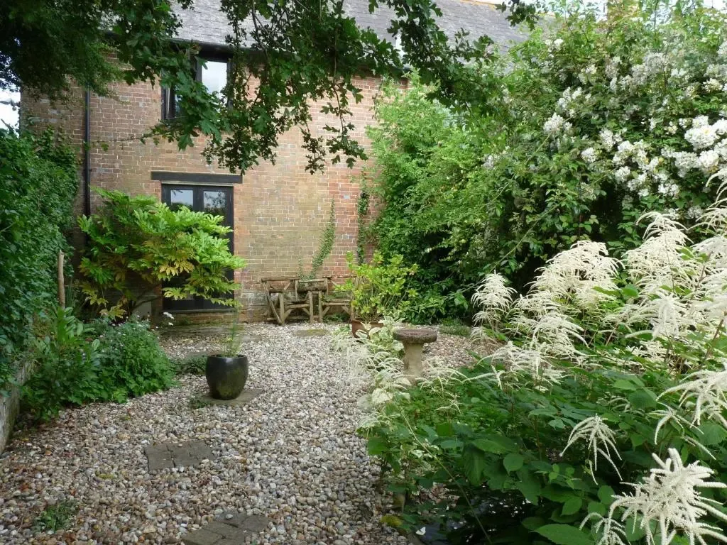 Un jardin fleuri avec une table et des bancs en bois près d'un bâtiment en briques.