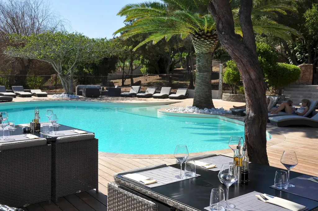 Tables dressées au bord d'une piscine ensoleillée avec des chaises longues.