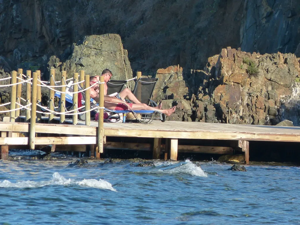 Deux personnes se relaxent sur des transats en bois au bord de l'eau.