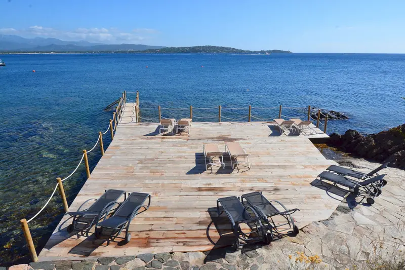 Terrasse en bois avec transats et tables au bord de la mer.