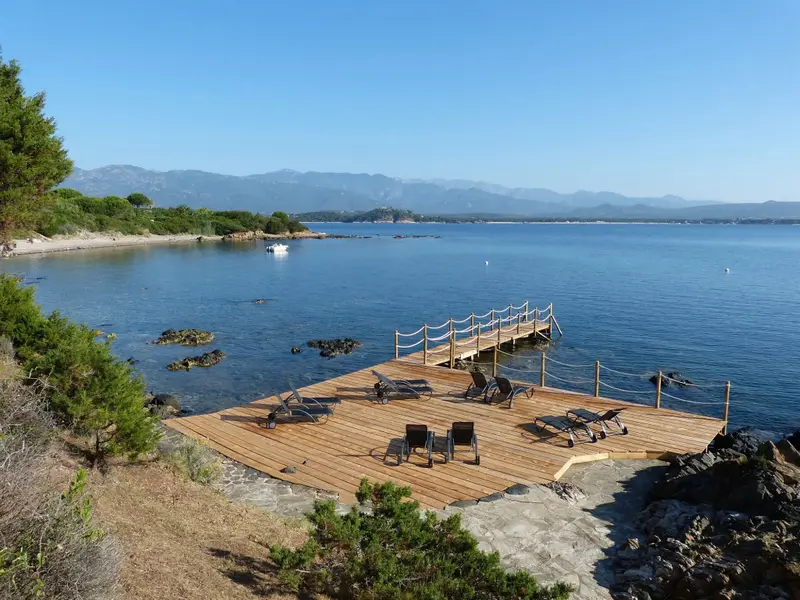 Plateforme en bois au bord de la mer avec des transats et une vue sur les montagnes.
