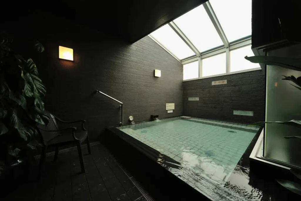 Une piscine intérieure sombre est éclairée par une verrière.