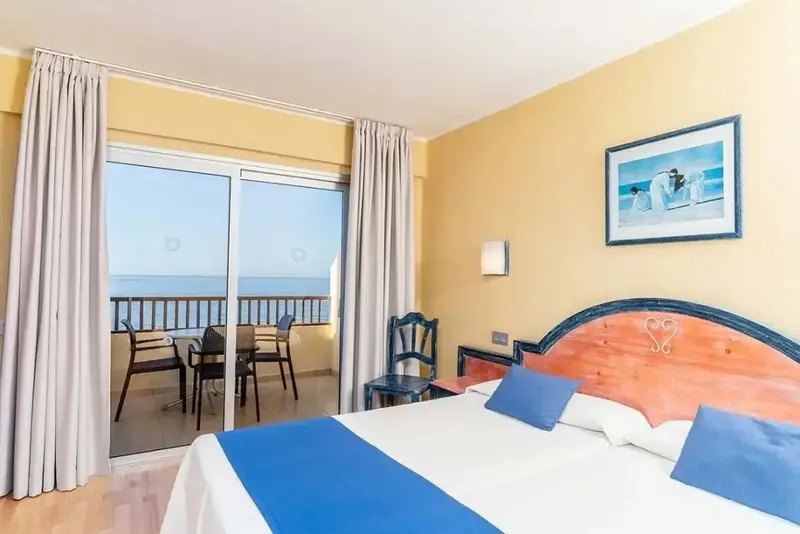 Une chambre lumineuse avec un grand lit donnant sur une terrasse et la mer.